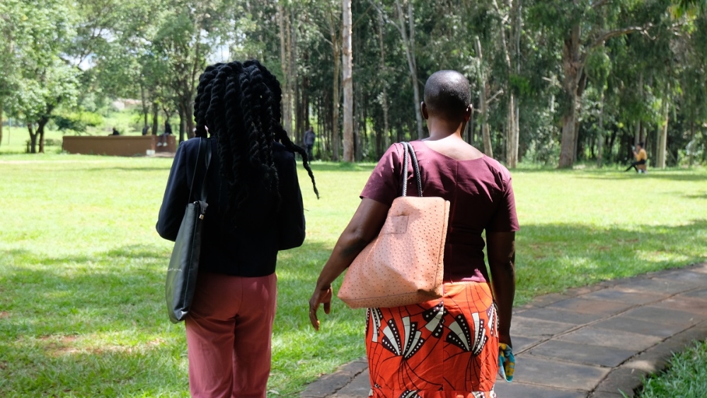 Two women walk through a green garden in a university campus with their backs to the camera.