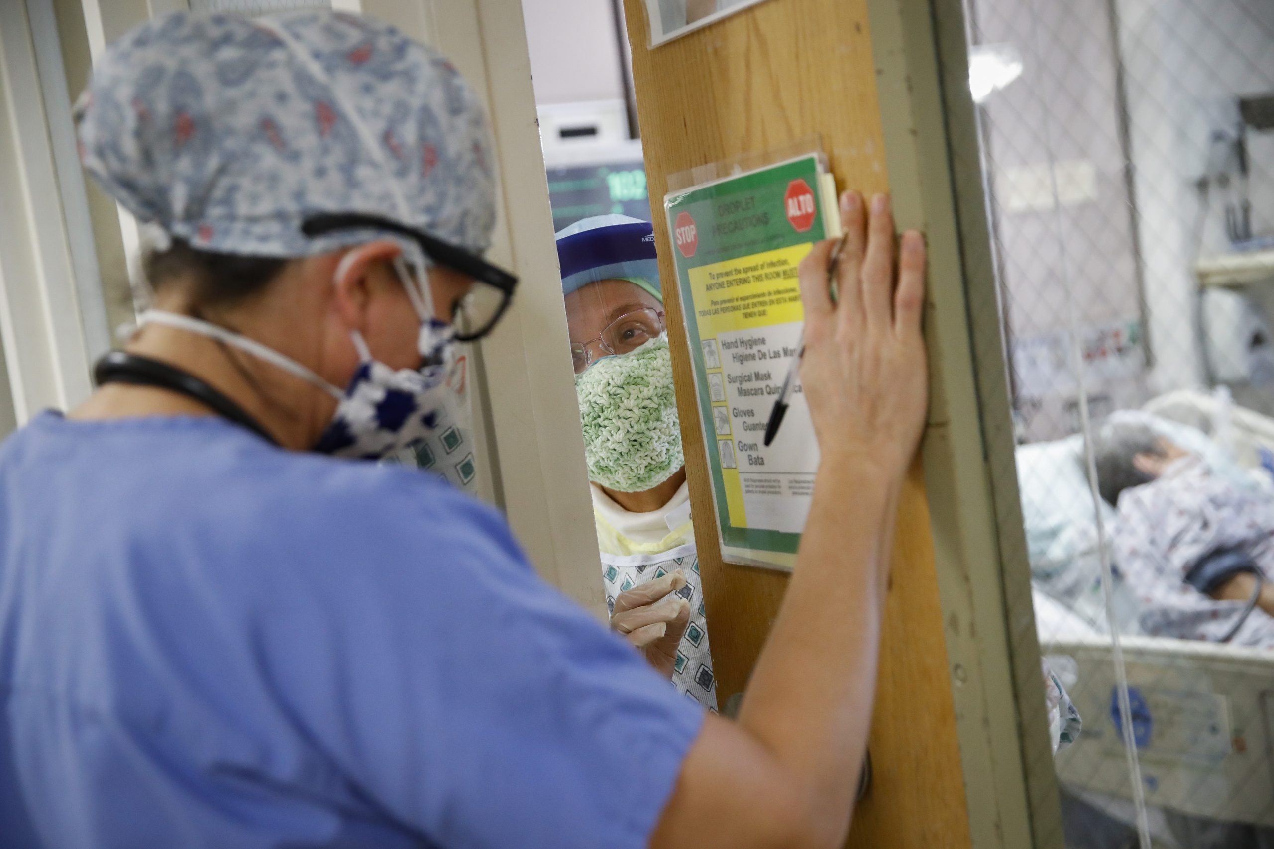 A nurse wearing a mask speaks to a physician wearing a mask inside an ICU