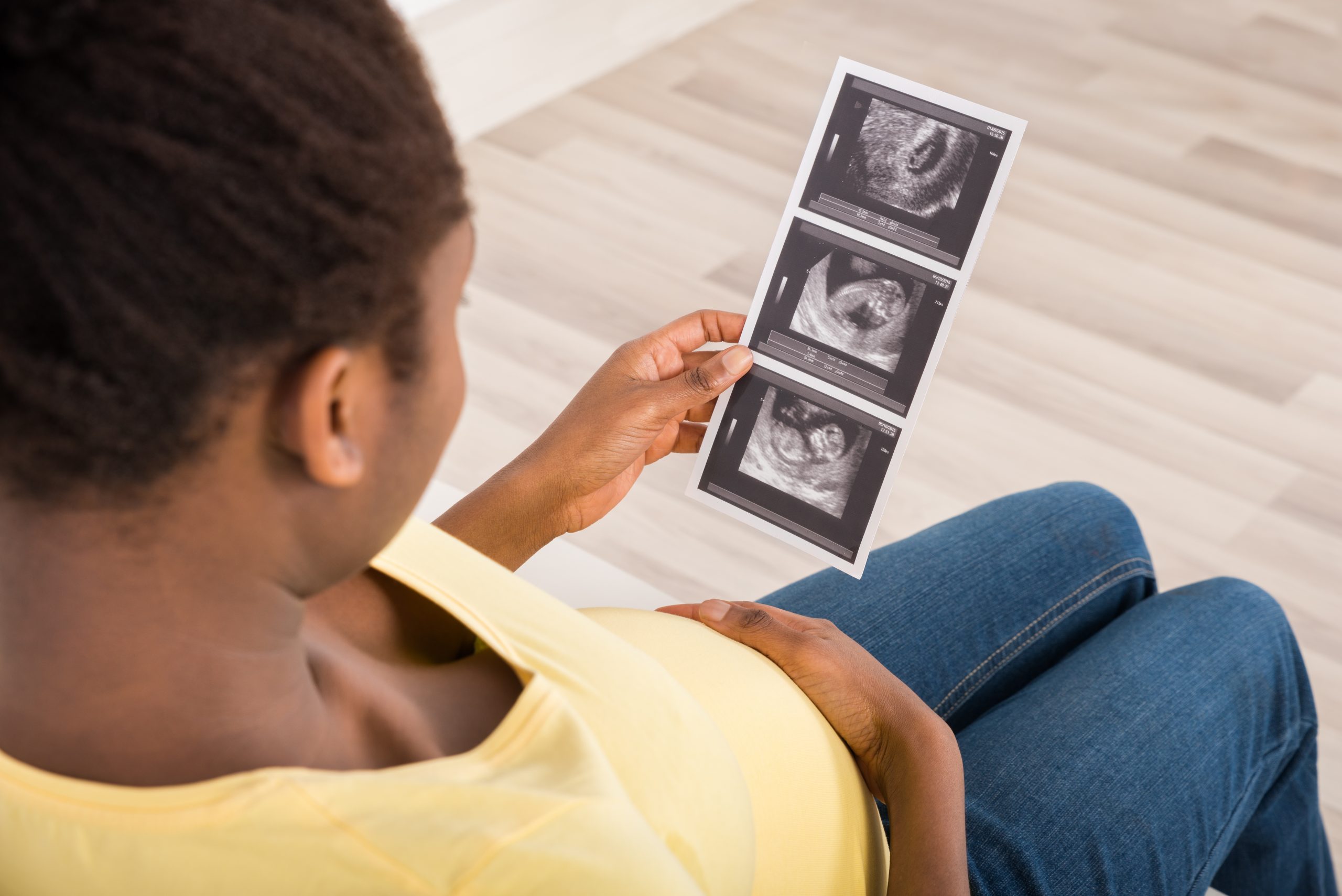 A pregnant woman wearing a yellow top looks at ultrasound scans of the baby