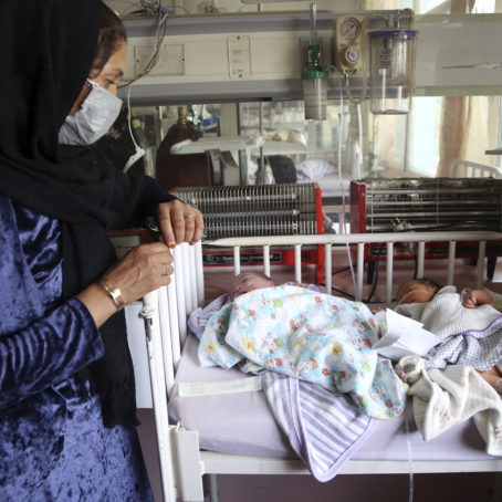 A woman wearing a hijab and a protective mask stands next to two newborn babies in the maternity ward of a hospital.