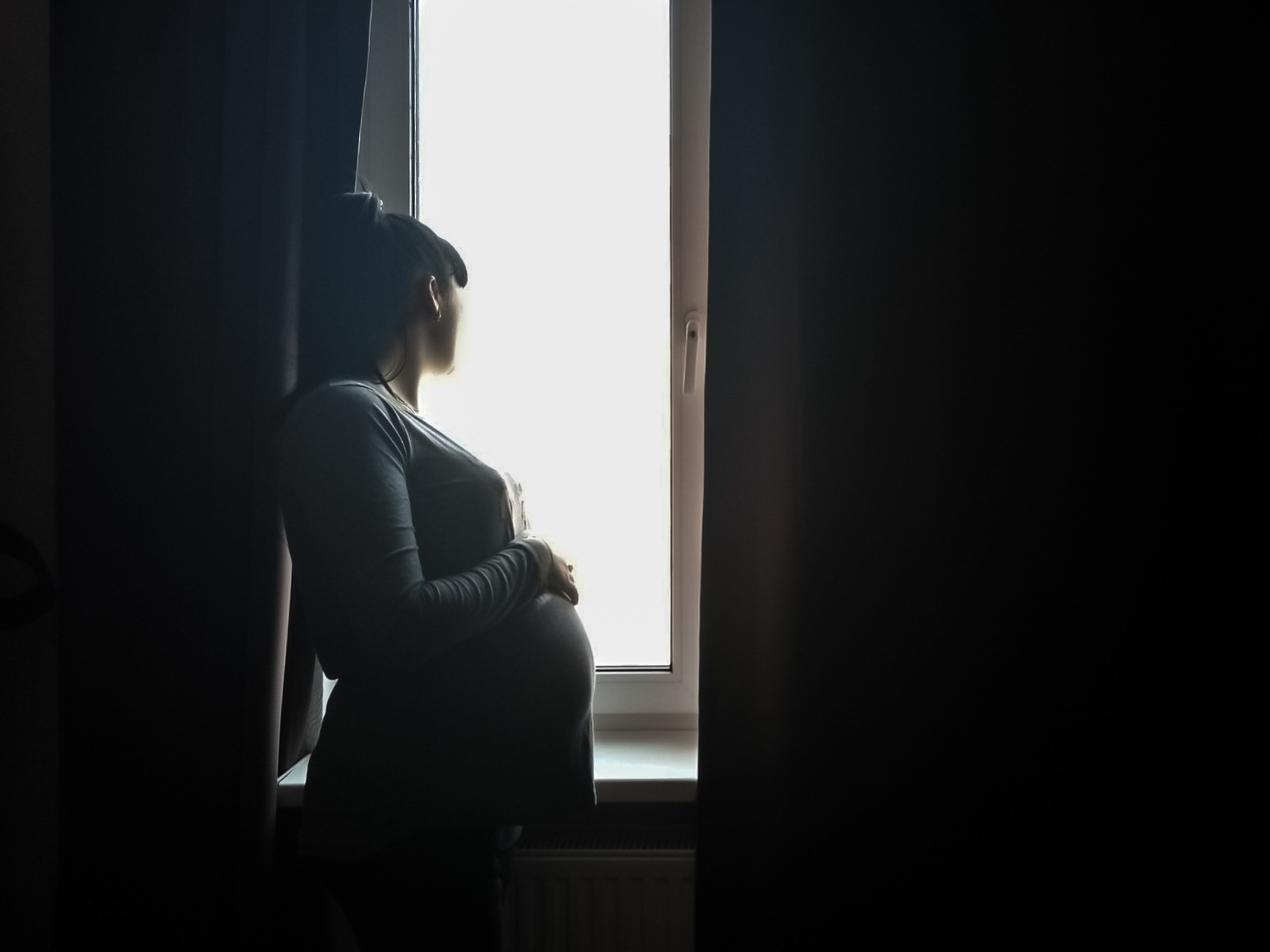 A heavily pregnant surrogate mother looks out of the window of her home.