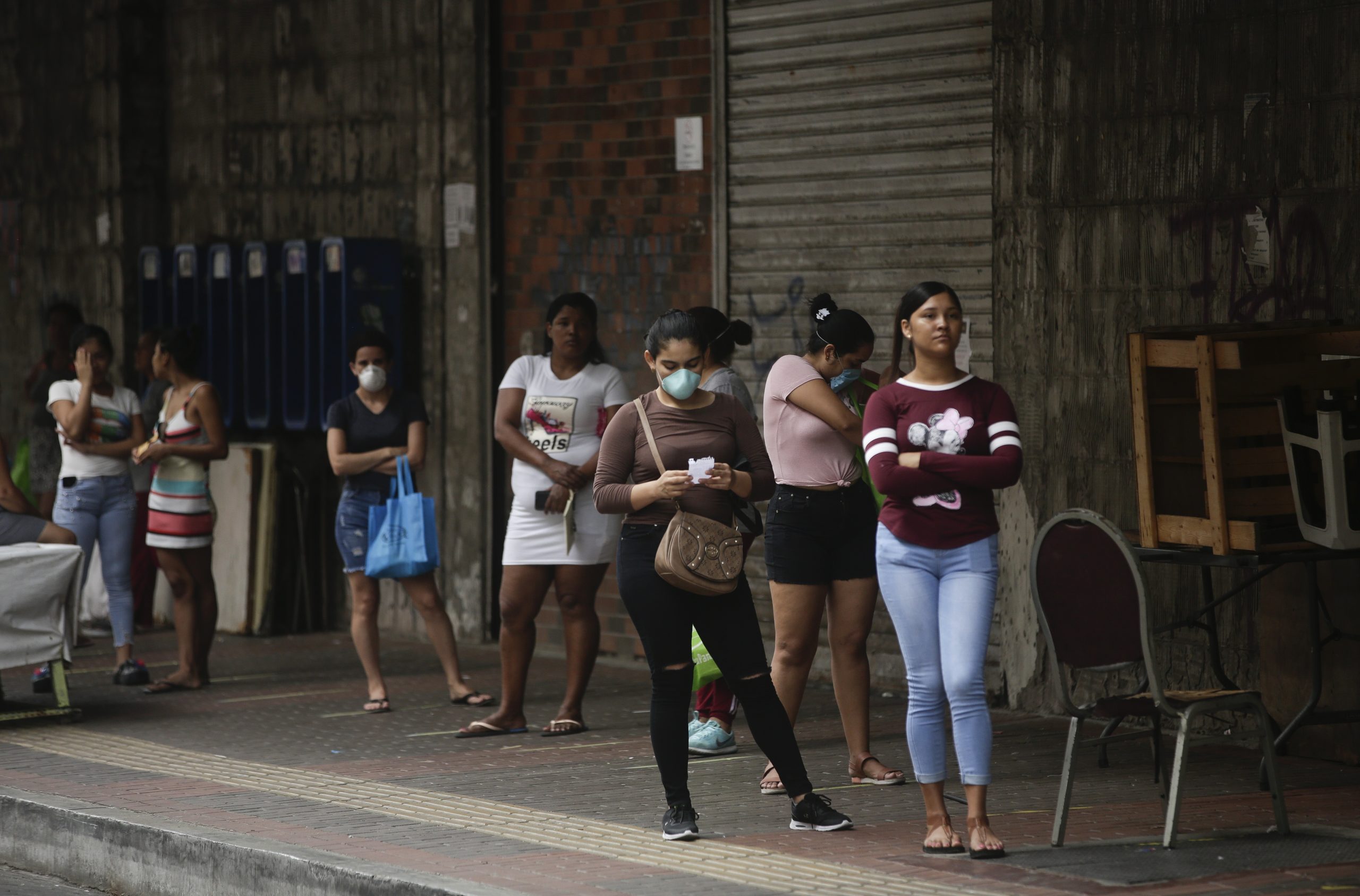 Women stand in line to enter a supermarket; some of them wearing a protective mask.