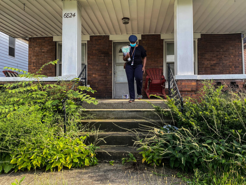A woman wearing a mask, walks down the front steps of a house