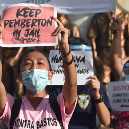 Demonstrators in Manila holding a poster with 'Keep Pemberton in jail' written on it; more posters in the background.