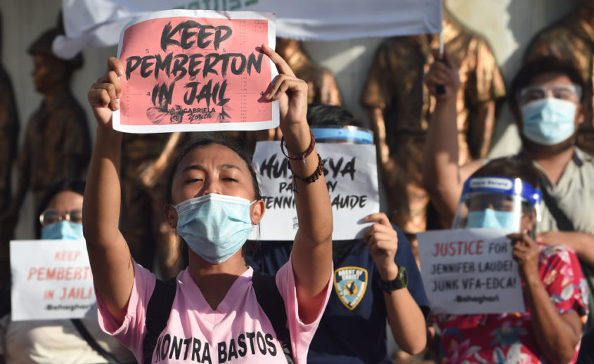 Demonstrators in Manila holding a poster with 'Keep Pemberton in jail' written on it; more posters in the background.