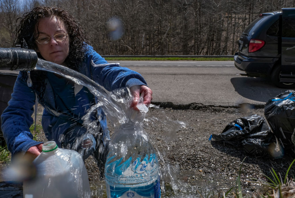 A photo of a woman filling up jugs of water from a water pump