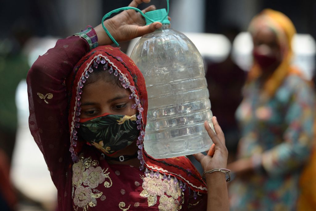 A photo of a woman as she balances a large plastic bottle of water on her shoulder