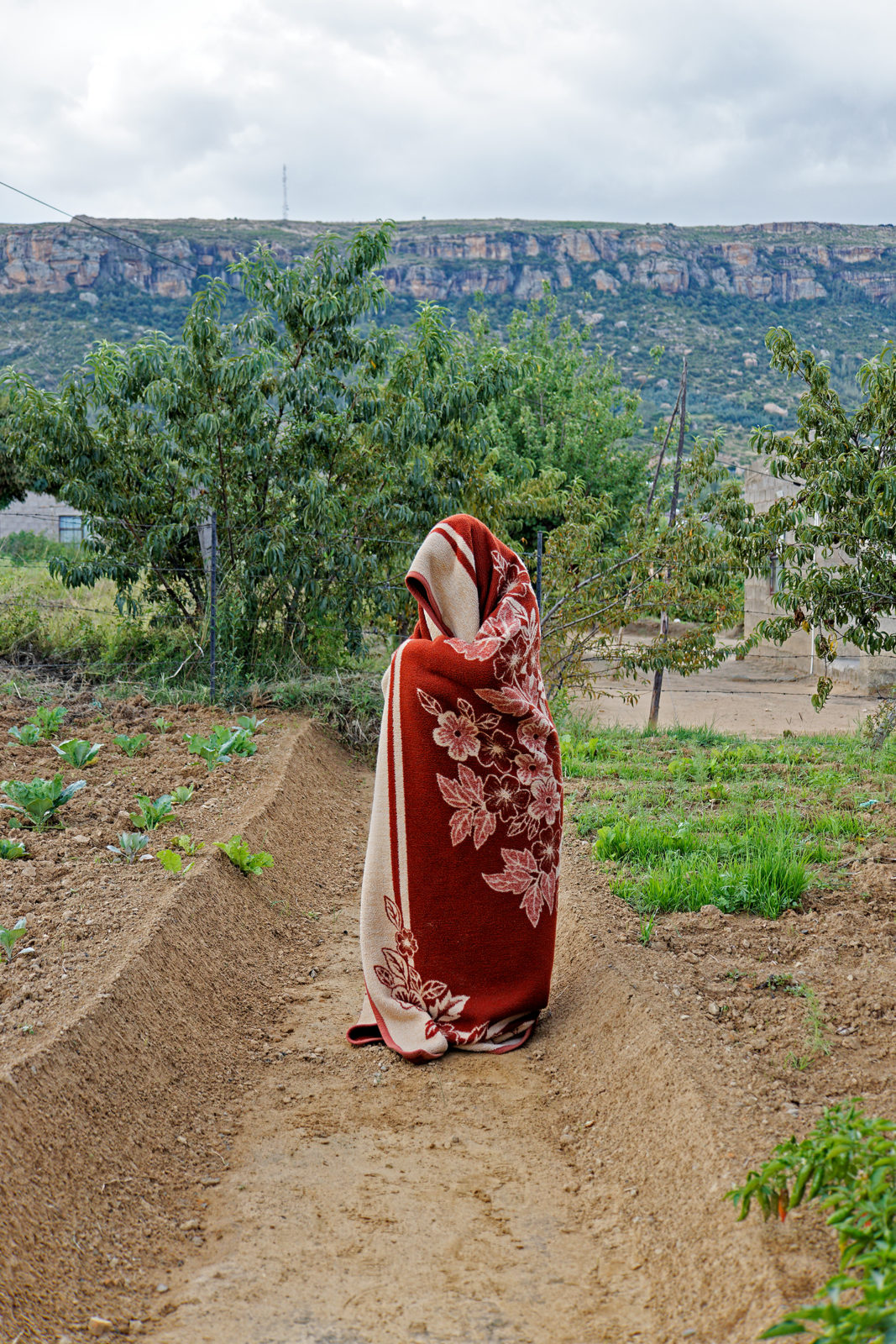 A photo of a cloaked person standing on a dirt road