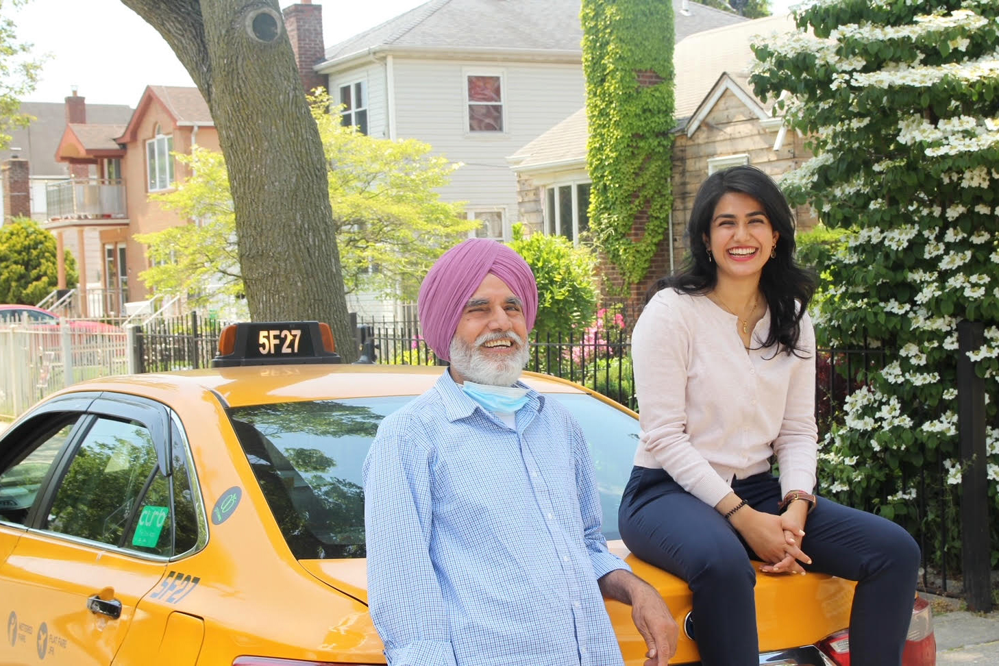 A photo of a man leaning on the back of a yellow cab, standing next to a woman, who is seated on the back of the cab