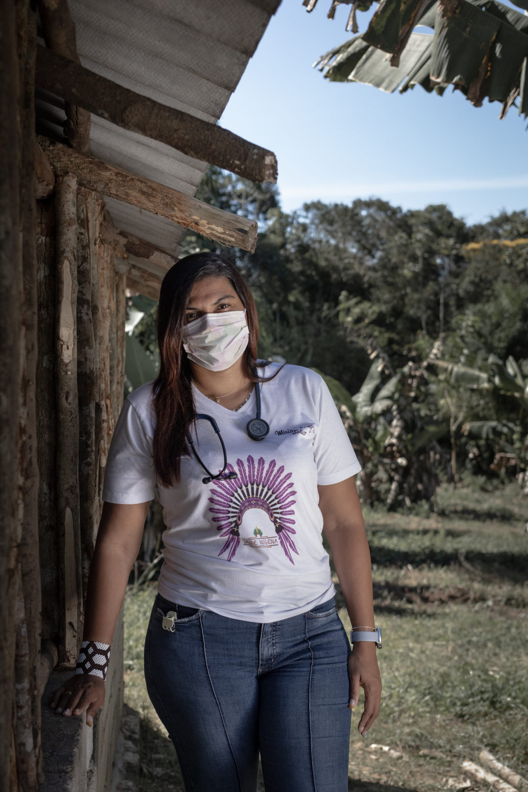 A photo of a doctor wearing a t-shirt, jeans and face mask at an Indigenous village
