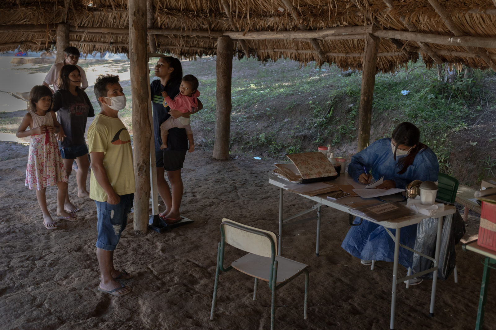 Photo of people standing in line to see a doctor beneath a thatched-roof structure