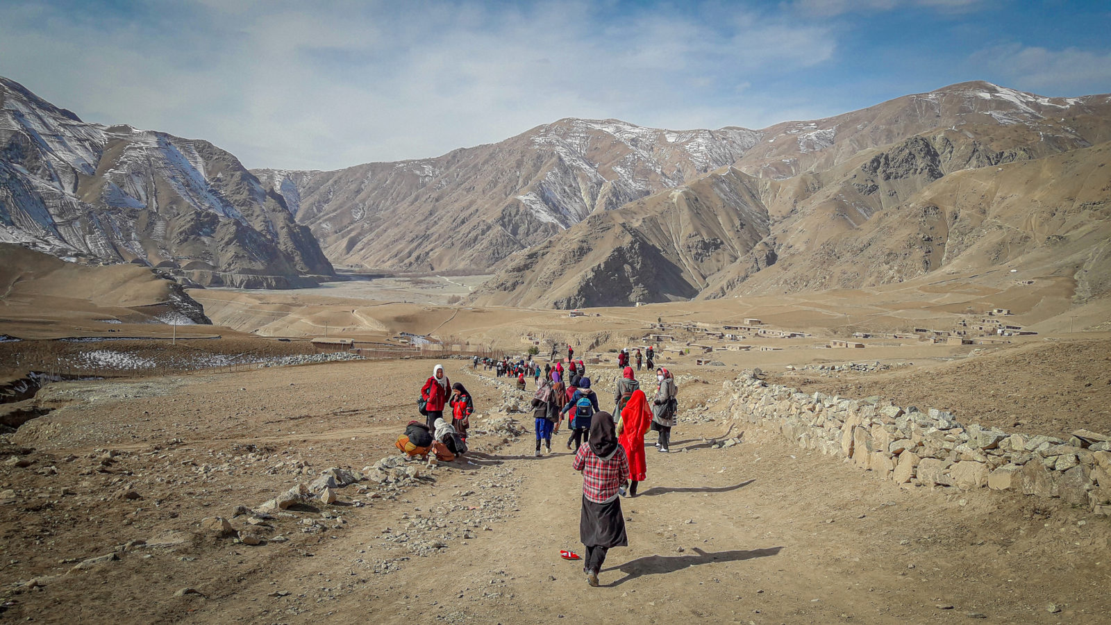 A photo of a group of girls walking along a dry dirt road with mountains in the backdrop