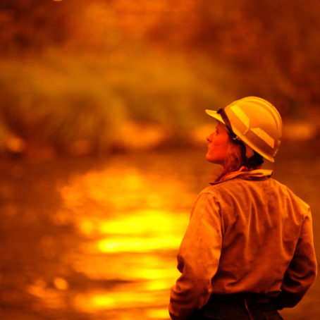 Photo of firefighter looking out at body of water reflecting flames