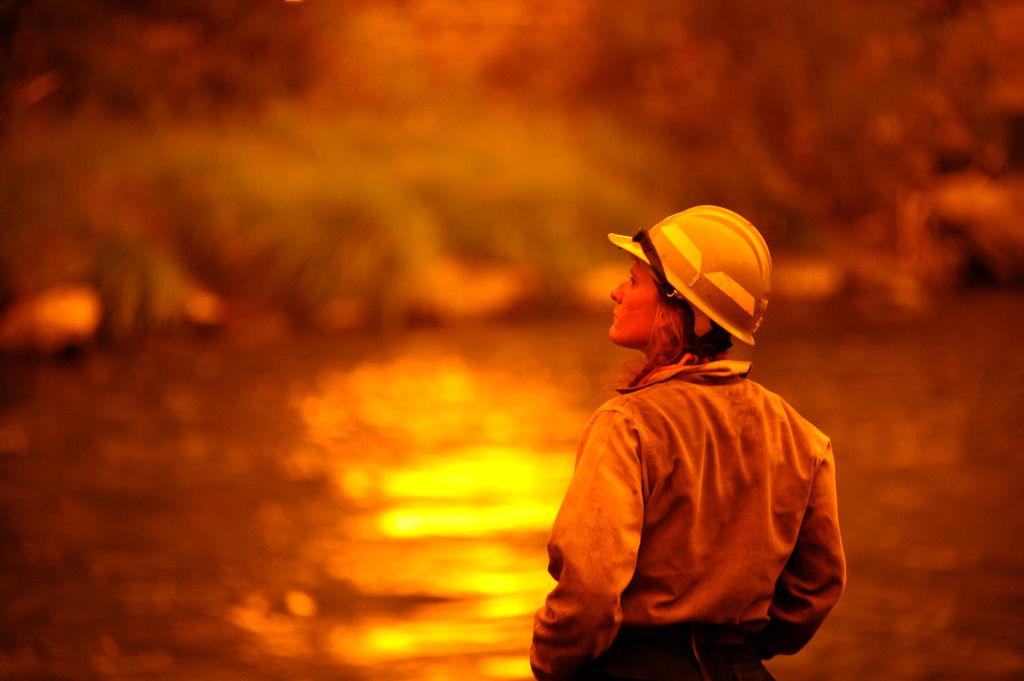 Photo of firefighter looking out at body of water reflecting flames