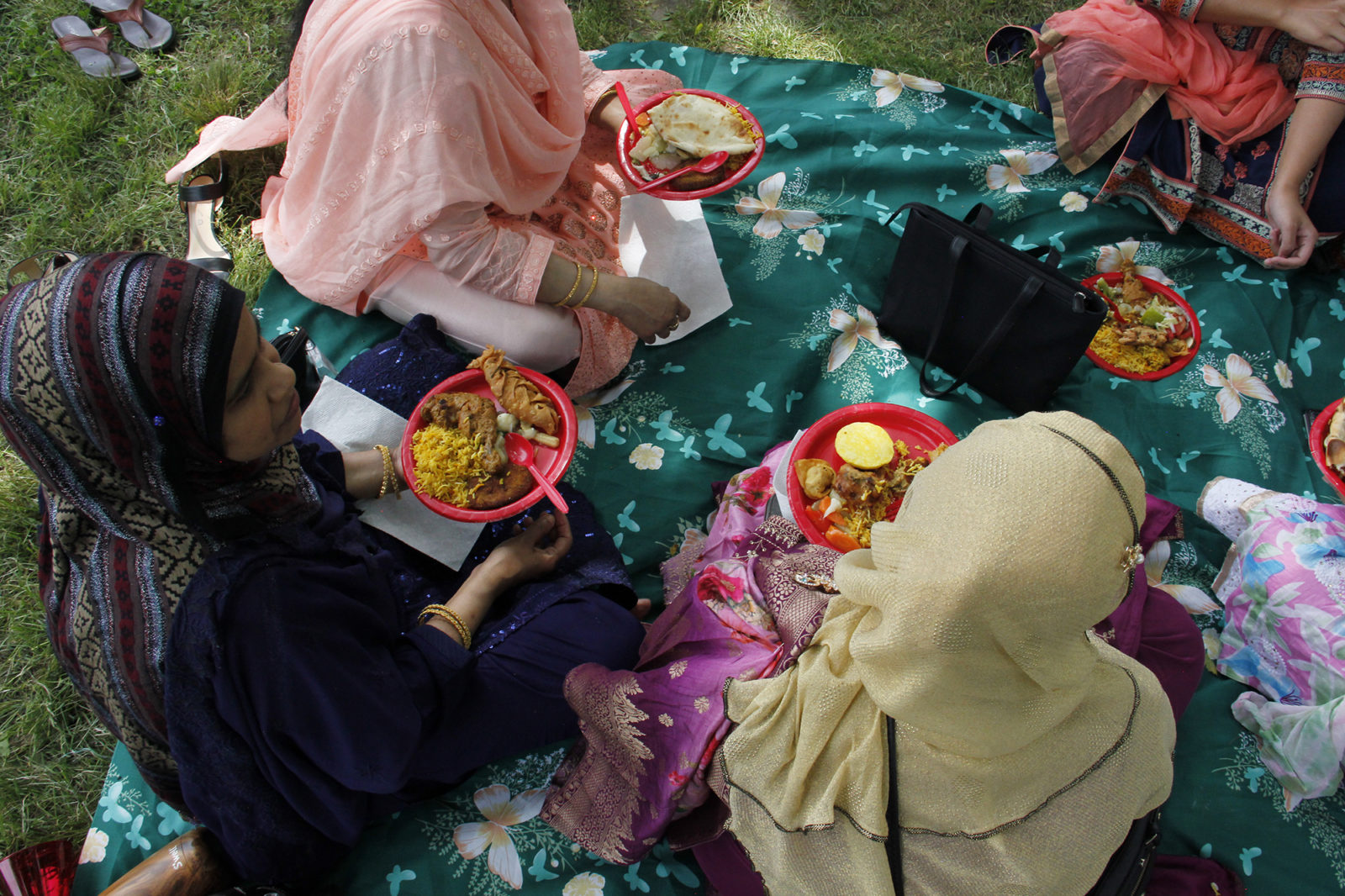 A photo of women on a blanket eating at an outdoor gathering