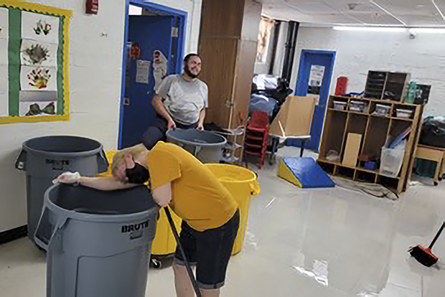 A photo of two people with plastic bins standing in a room with a flooded floor