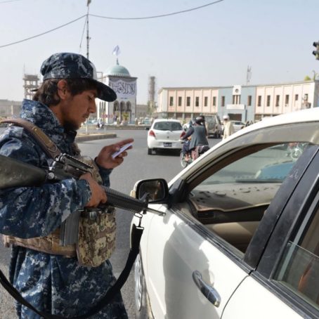 A photo of a Taliban soldier pointing a weapon at a driver at a checkpoint