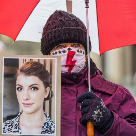 Photo of a protestor holding a woman's photo and a large red umbrella