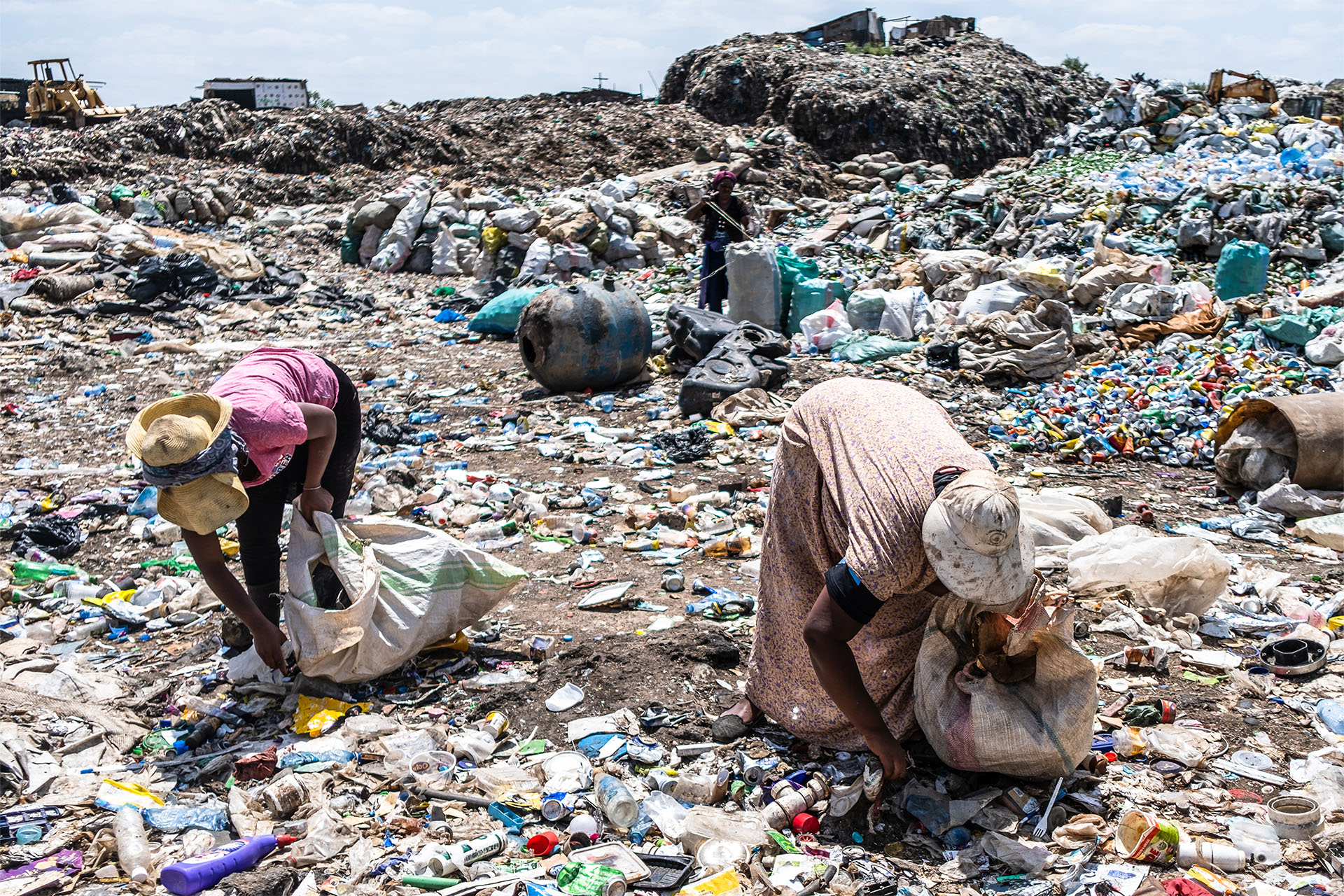 A photo of two women picking up trash at a dumpsite