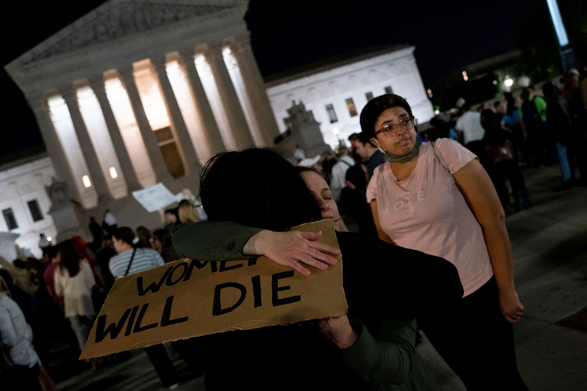 A photo of two people hugging holding a sign that says "women will die"