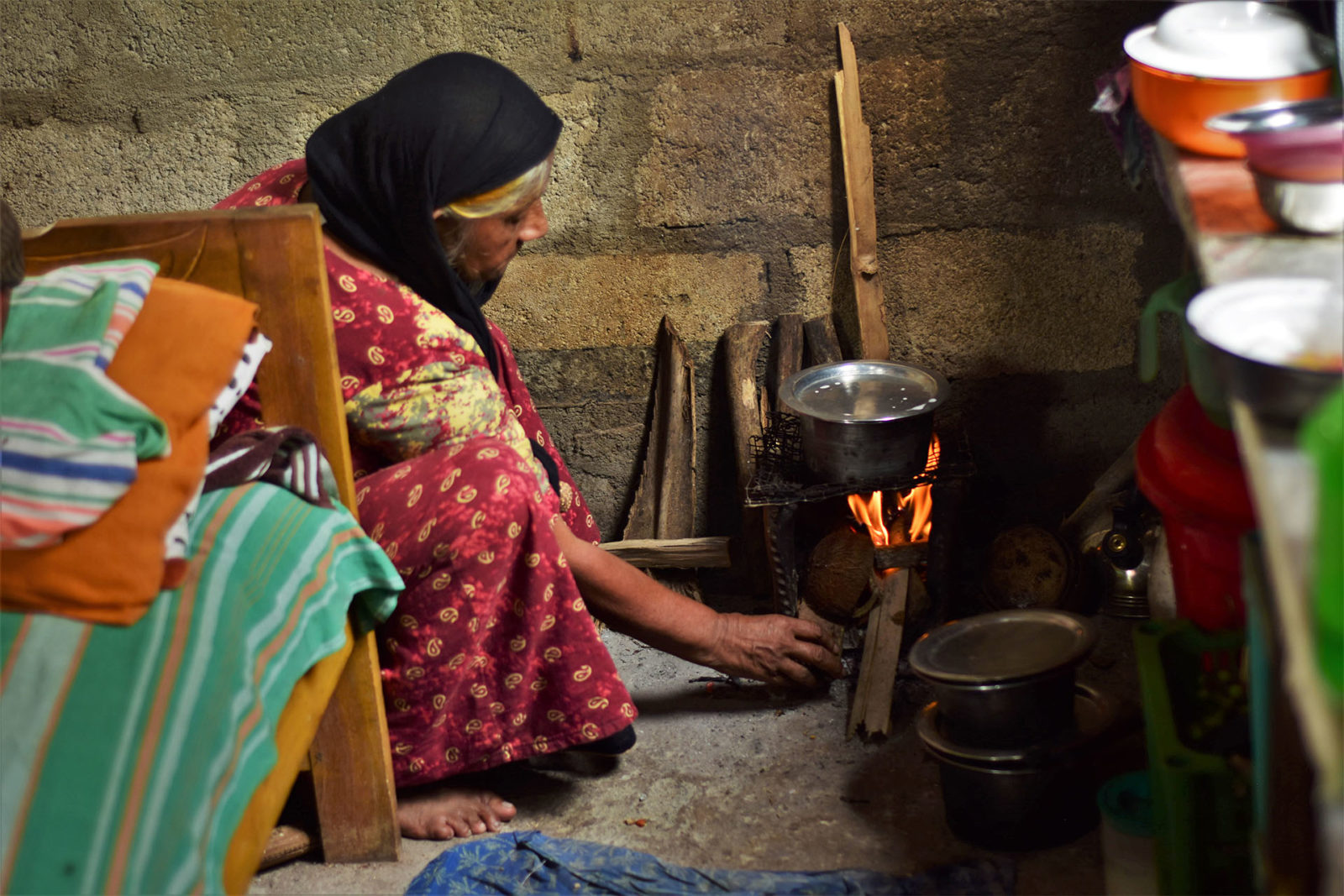 Photo of a woman heating fire wood beneath a pot inside a room