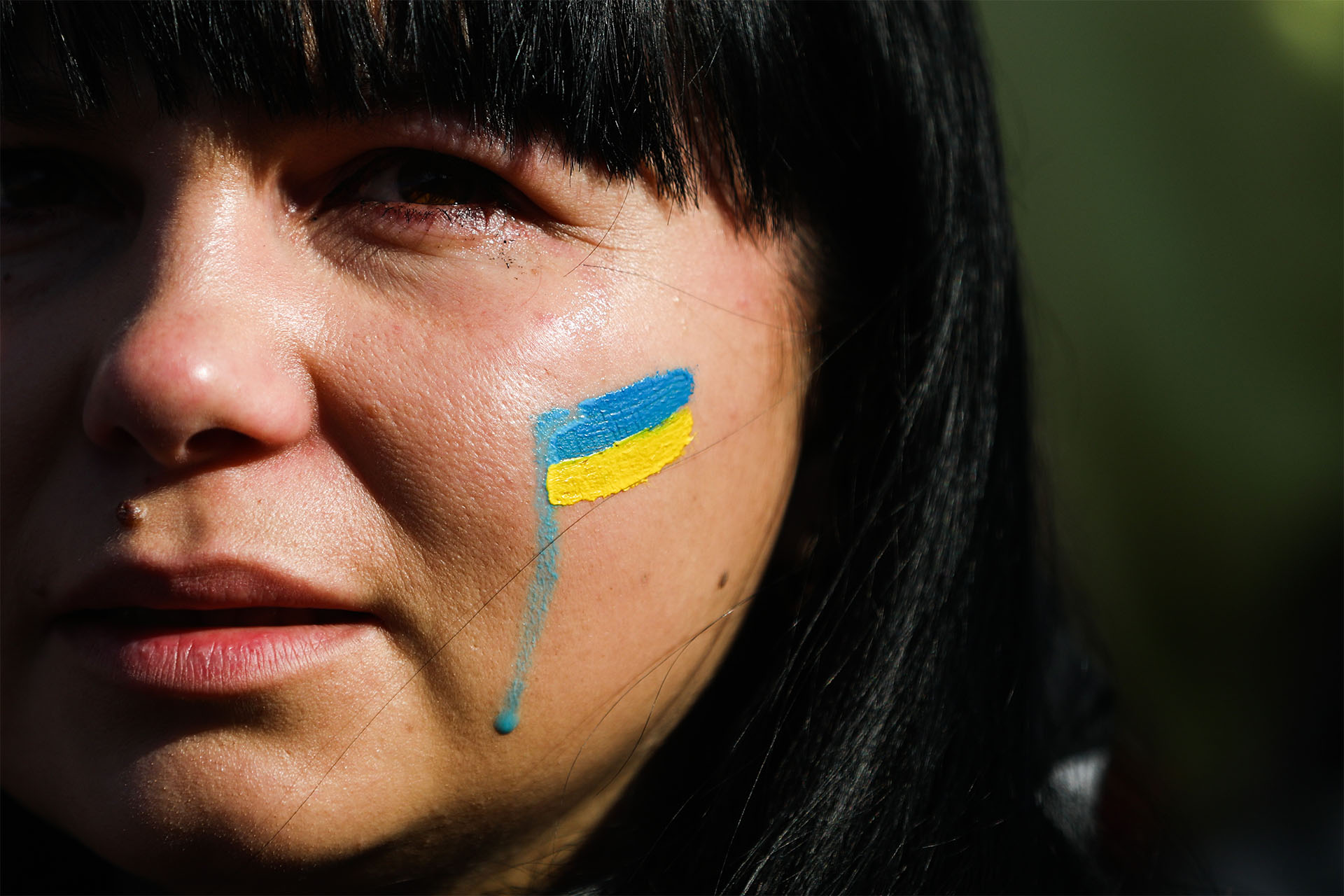 Photo of a woman's face with a tear smearing a painted Ukrainian flag on her cheek
