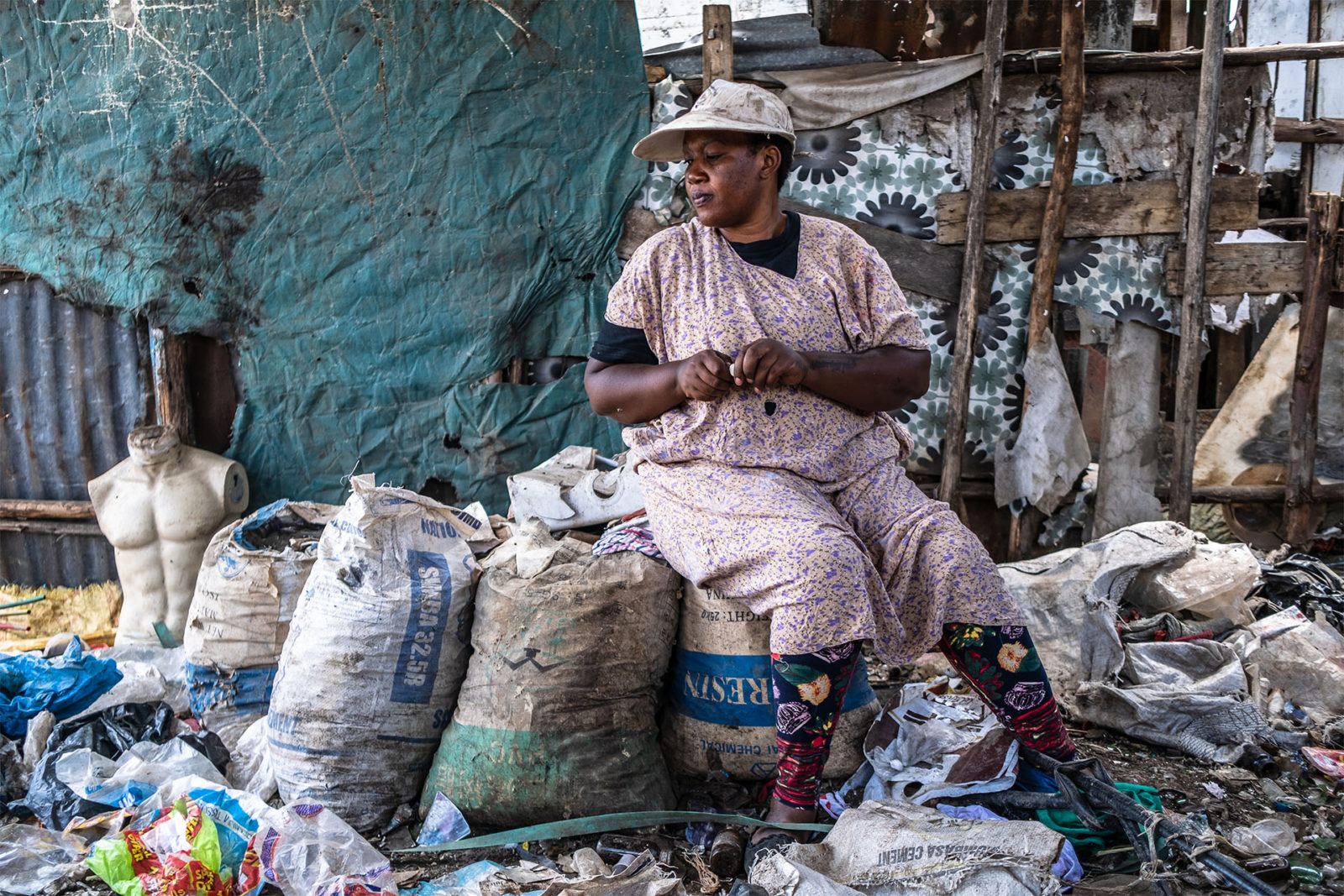 A photo of a woman sitting on bags of trash at a dumpsite