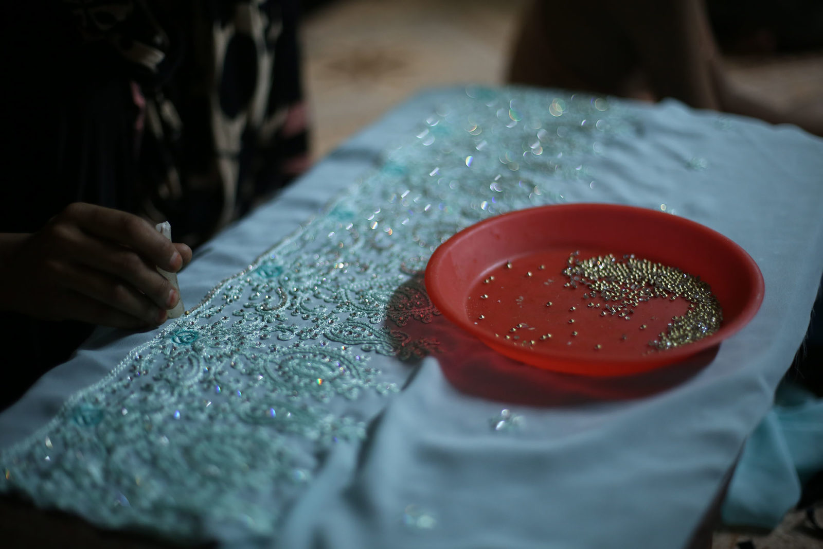 A photo of a person applying beads on an embroidered cloth