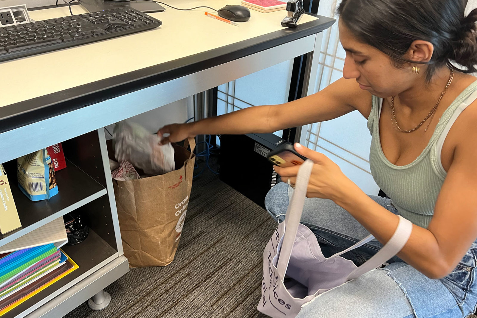 A photo of a person crouching under a desk putting something in a bag