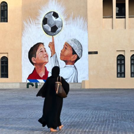 A woman walks past a mural of two boys looking up at a soccer ball.