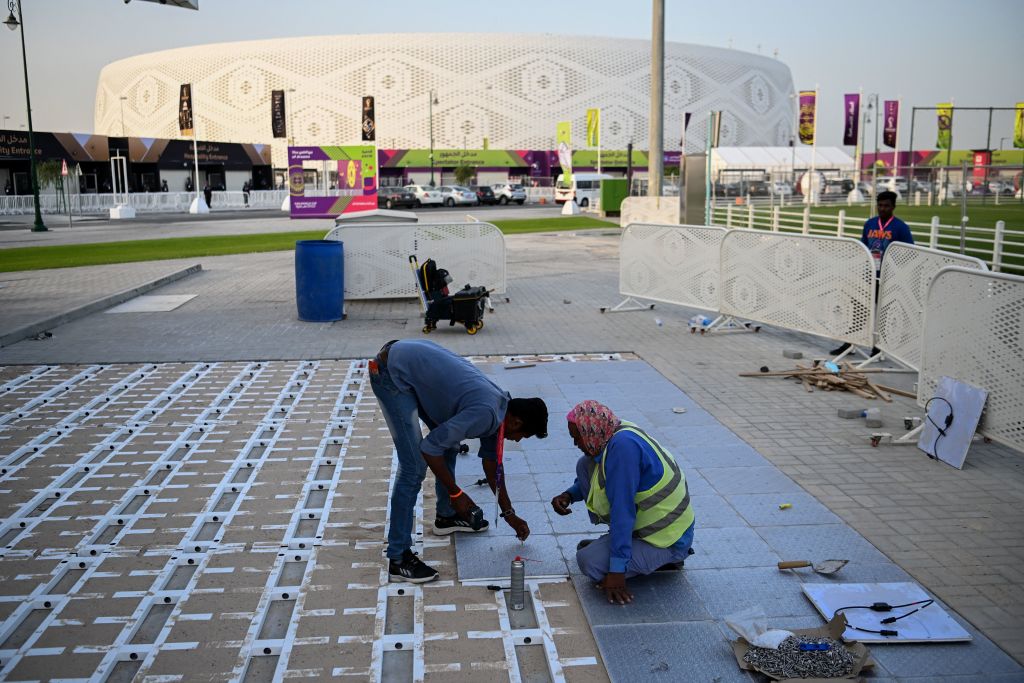 Men work outside on a concrete floor in front of a soccer stadium.