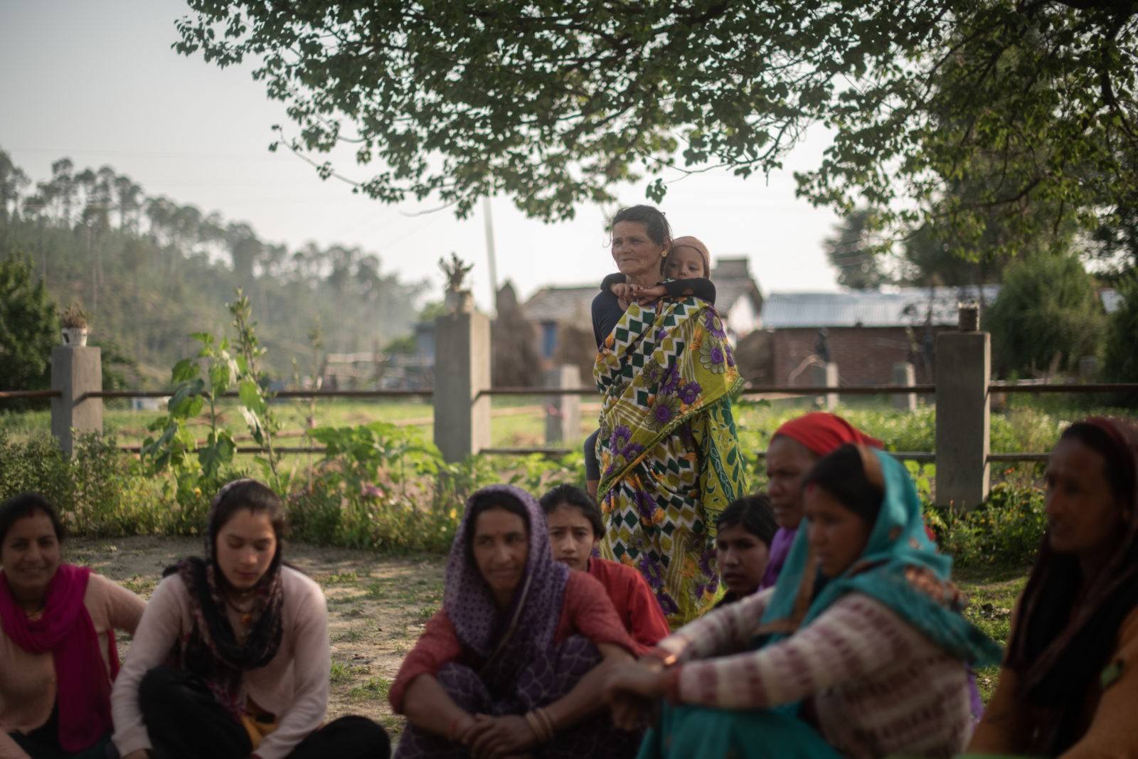 A group of women sit together on the ground in their village.