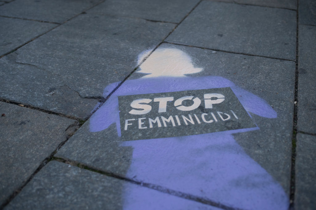 An image of a woman spray painted on the ground holding a sign that says "Stop Femminicidi"