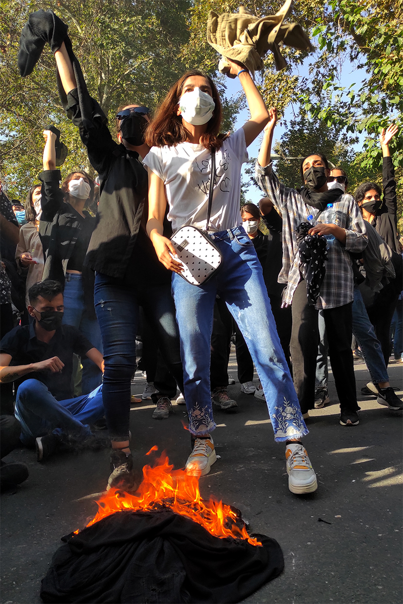 Iranian women stand in front of a pile of scarves on fire.