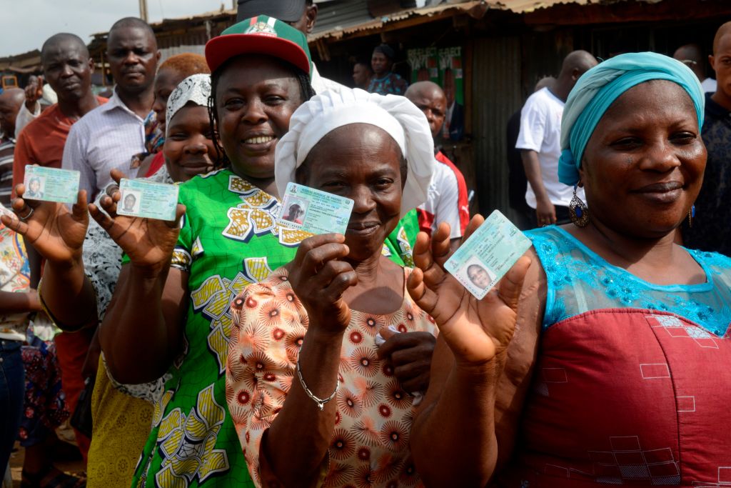 Women voters stand in line showing their voter ID cards.