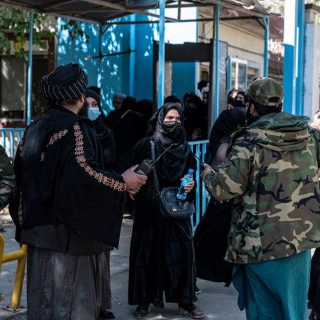 Taliban fighters stand in front of female students at a blue door.