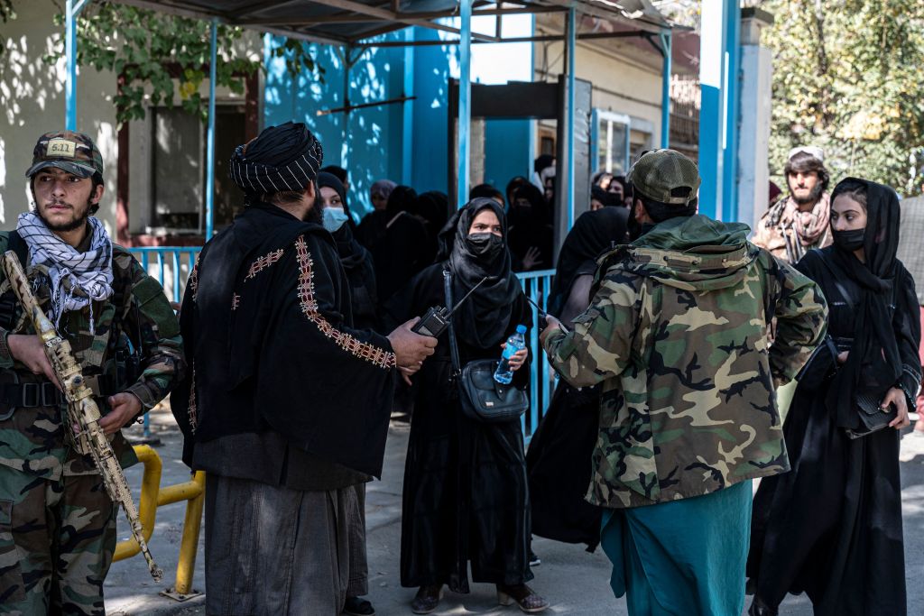 Taliban fighters stand in front of female students at a blue door.