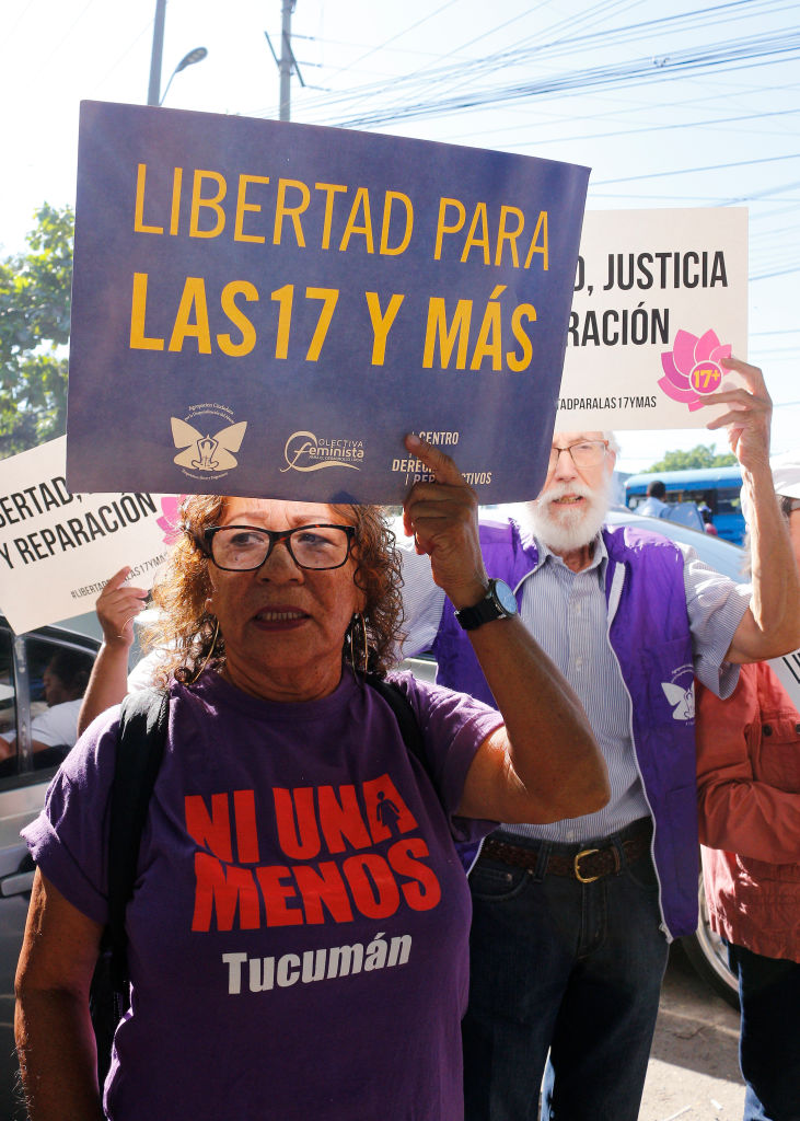 A woman and a man stand while holding signs that say libertad para las y mas
