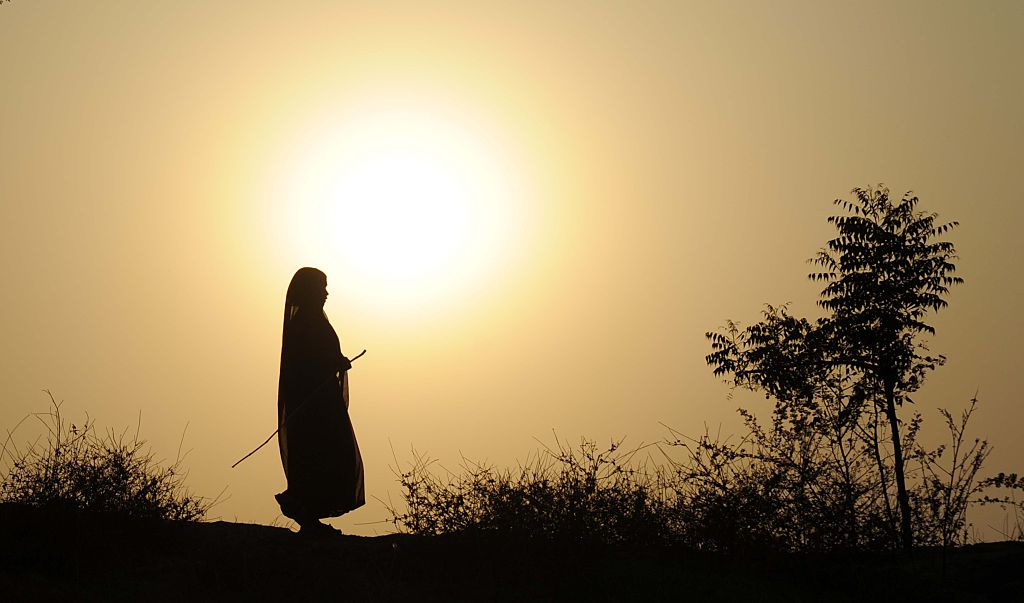 A woman walks across a dried up river with the sun shining yellow in the background.