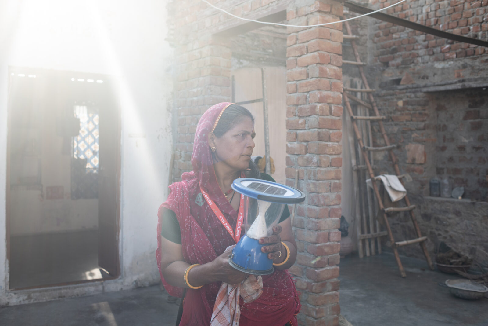 A woman holds a blue solar lamp while standing in the sun.