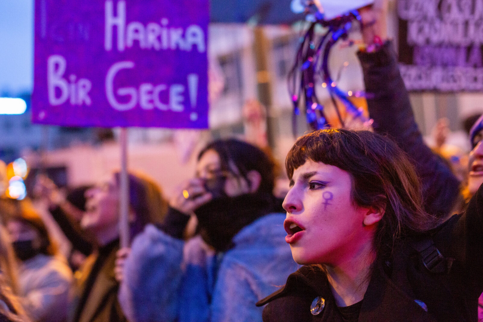 A woman shouts at a protest with the symbol for females painted in purple on her cheek.