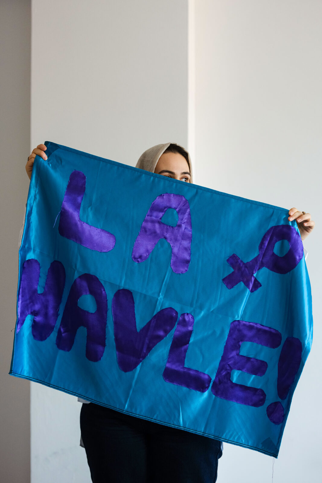 A woman stands holding a blue sign that says "La Halve" in purple letters.
