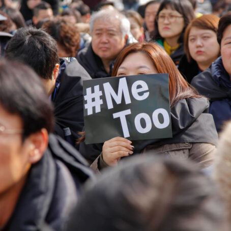 A woman covers her face with a #MeToo sign while sitting on the ground.