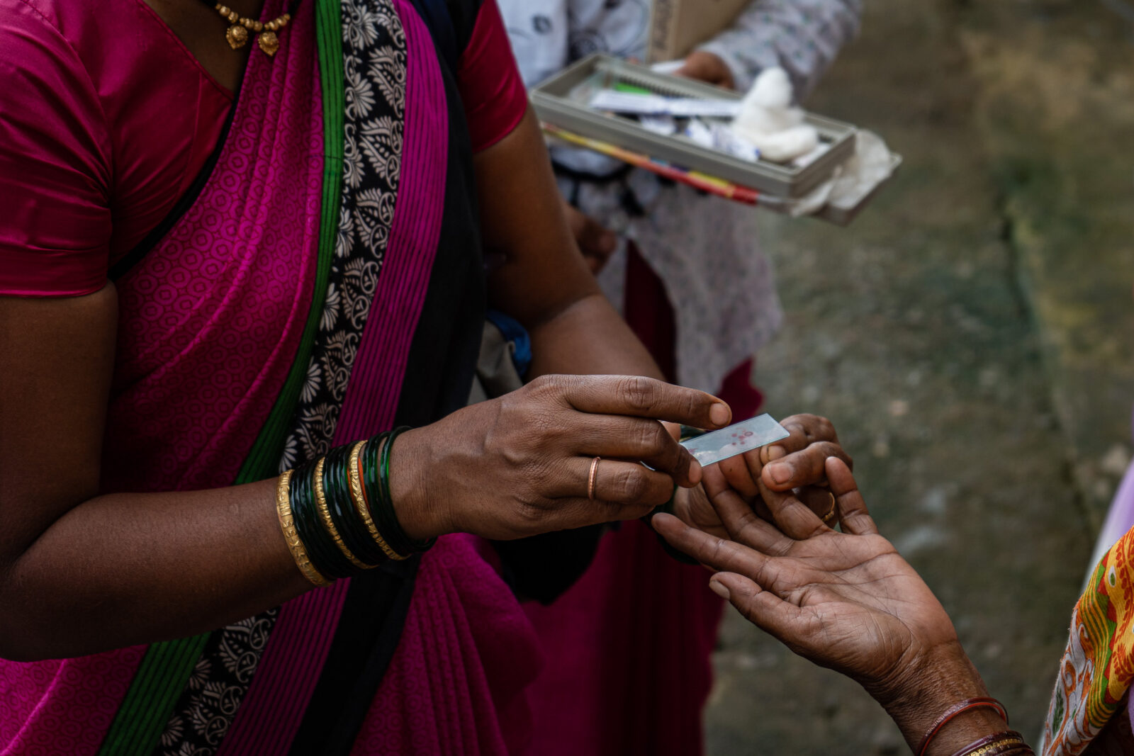 A woman collects a blood sample from another woman's hand.